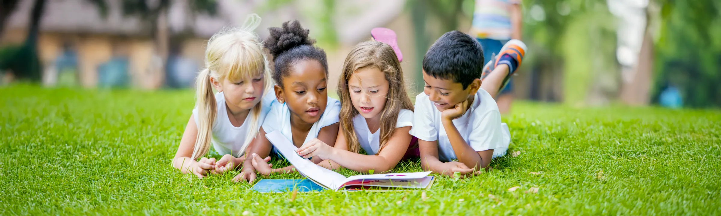 Children lying on the grass, engaging together in a story book